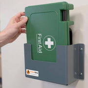 Green first aid kit in gray wall mount with white cross and hand pulling it out | PicSEO 1789750205510